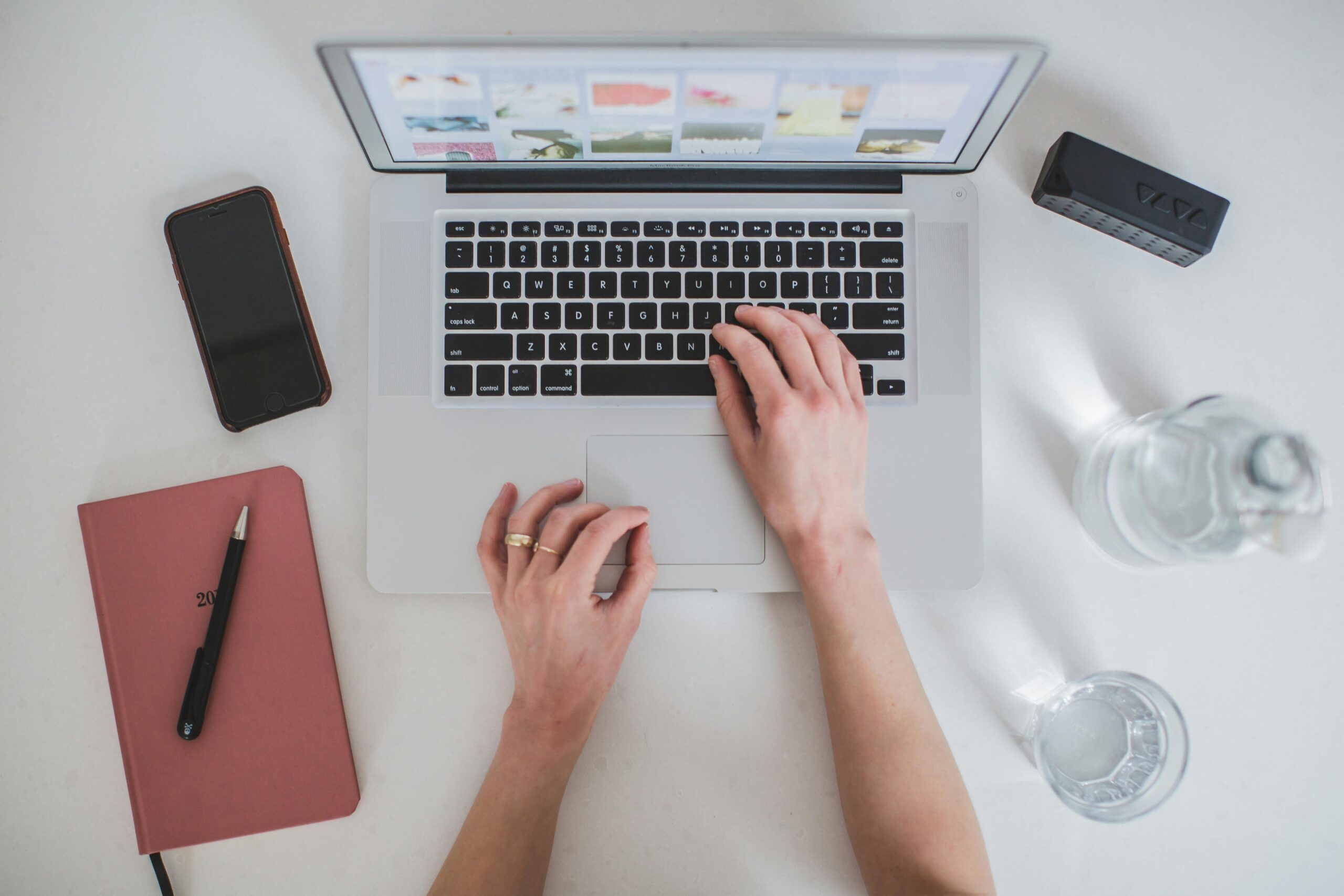 hands typing on a laptop with a webpage open, working on landing pages, surrounded by a notebook, phone, and water bottle on a clean white desk